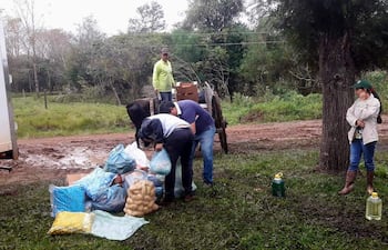 Grupo de cinco personas en un ambiente rural; un hombre con sombrero supervisa un carro, mientras otros manipulan bolsas de alimentos.