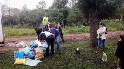 Grupo de cinco personas en un ambiente rural; un hombre con sombrero supervisa un carro, mientras otros manipulan bolsas de alimentos.