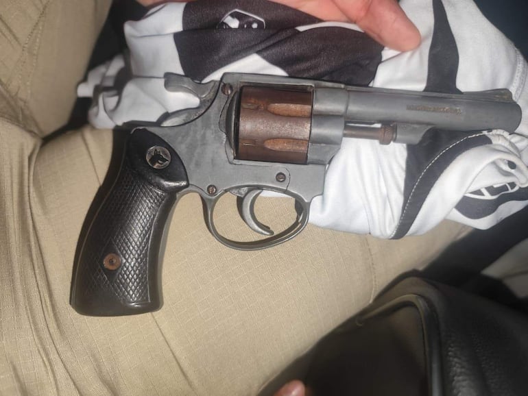 Revólver en mano sobre prenda blanquinegra; el arma presenta detalles visibles como empuñadura y cilindro.