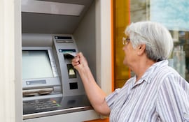 Una mujer de la tercera edad retira dinero de un cajero automático.