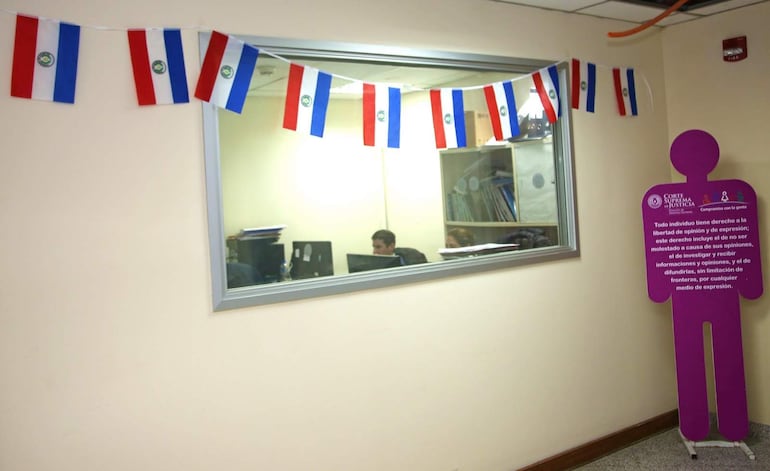 Banderas de Paraguay decoran el entorno, mientras un cartel sobre libertad de expresión resalta en el ambiente legal.