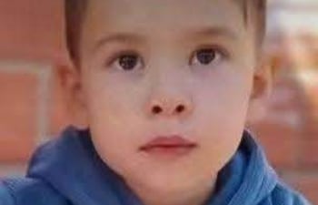 Khael Valdez, niño de 3 años, sentado con hoodie azul y pantalones naranjas, sostiene un vaso blanco en un entorno tranquilo.