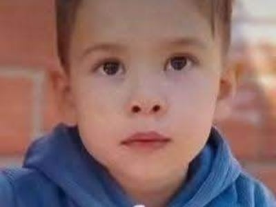 Khael Valdez, niño de 3 años, sentado con hoodie azul y pantalones naranjas, sostiene un vaso blanco en un entorno tranquilo.