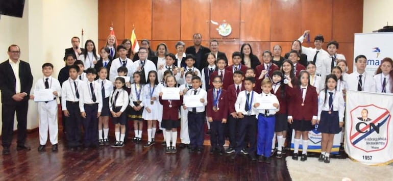 Grupo de niños con medallas y certificados en un ambiente festivo, algunos adultos observan y apoyan la premiación.