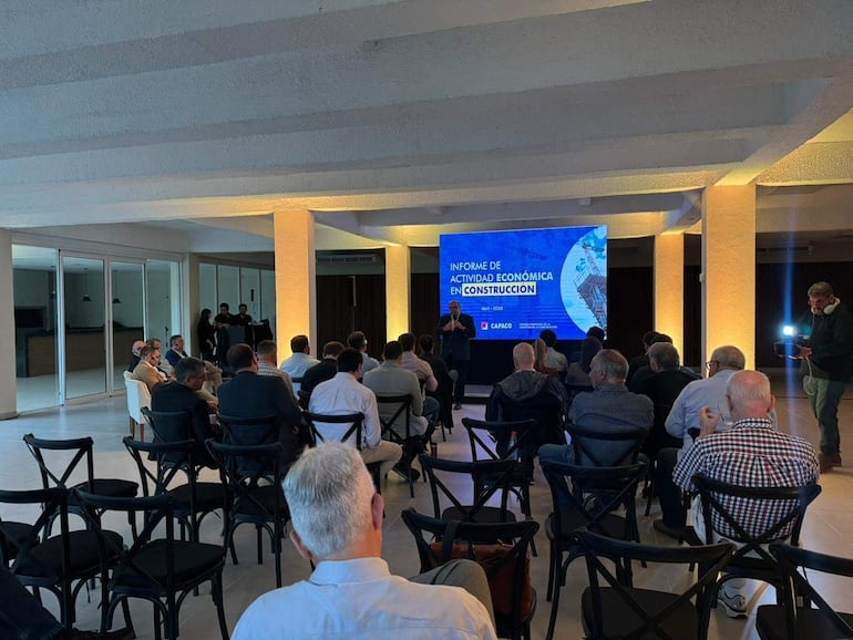 Hombre de pie presenta en un salón a unos 30 asistentes. Pantalla muestra 'INFORME DE ACTIVIDAD ECONÓMICA EN CONSTRUCCIÓN' de CAPACO.