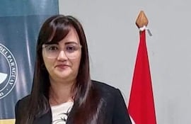 Librada Beatriz Peralta Céspedes, en atuendo formal negro, sostiene un diploma frente a banderas de Paraguay y de la universidad.