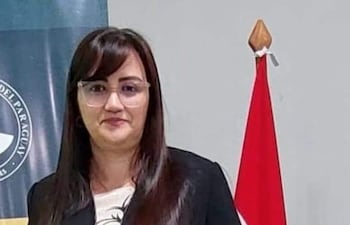 Librada Beatriz Peralta Céspedes, en atuendo formal negro, sostiene un diploma frente a banderas de Paraguay y de la universidad.