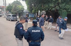 Grupo de policías en uniformes, conversando en la calle. Uno lleva chaleco táctico. Iluminación nublada.