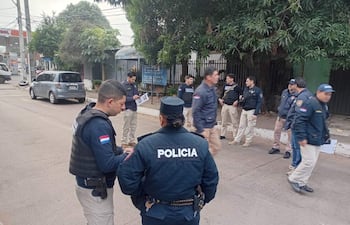 Grupo de policías en uniformes, conversando en la calle. Uno lleva chaleco táctico. Iluminación nublada.