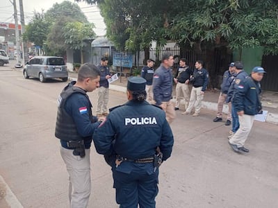 Grupo de policías en uniformes, conversando en la calle. Uno lleva chaleco táctico. Iluminación nublada.