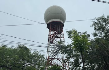 Torre de comunicación alta y metálica, con esfera blanca en su cima, rodeada de árboles y cables eléctricos.