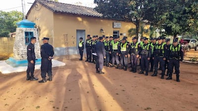 Policías en uniforme oscuro y chalecos amarillos, alineados en formación, conversando en un entorno rural.