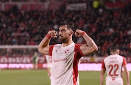 Jugador de Independiente con camiseta blanca y roja en actitud celebratoria; otros jugadores y un público animado en el fondo.