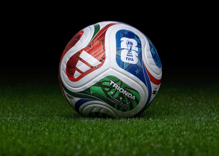 Balón oficial de la Copa del Mundo sobre césped, con diseño vibrante que incluye el logotipo de Adidas y emblema de la FIFA.