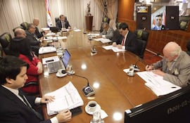 Víctor Ríos Ojeda y Alberto Martínez Simón junto a otros en mesa, todos con trajes formales, analizando documentos en ambiente sobrio.