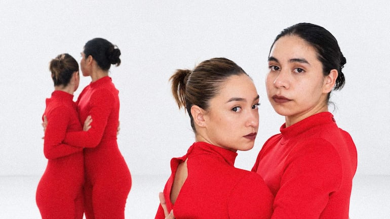 Dos mujeres en trajes rojos posan en un fondo blanco, una mira hacia atrás y la otra a la cámara con expresión tranquila.