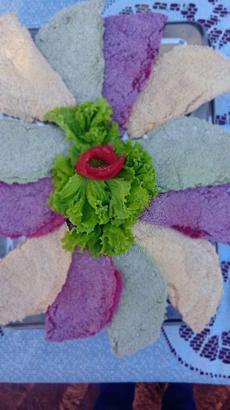 Plato decorativo de empanadas de varios colores, con lechuga y pimiento rojo en un fondo azul.
