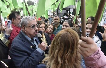 Isaías Fretes, mayor con gafas y micrófono, rodeado de mujeres y hombres con banderas verdes y pancartas durante la manifestación.