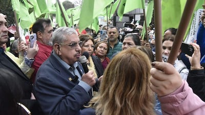 Isaías Fretes, mayor con gafas y micrófono, rodeado de mujeres y hombres con banderas verdes y pancartas durante la manifestación.