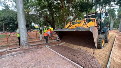 Hombre con chaleco naranja y casco amarillo opera maquinaria en construcción, rodeado de otros trabajadores con chalecos neón y cascos blancos.