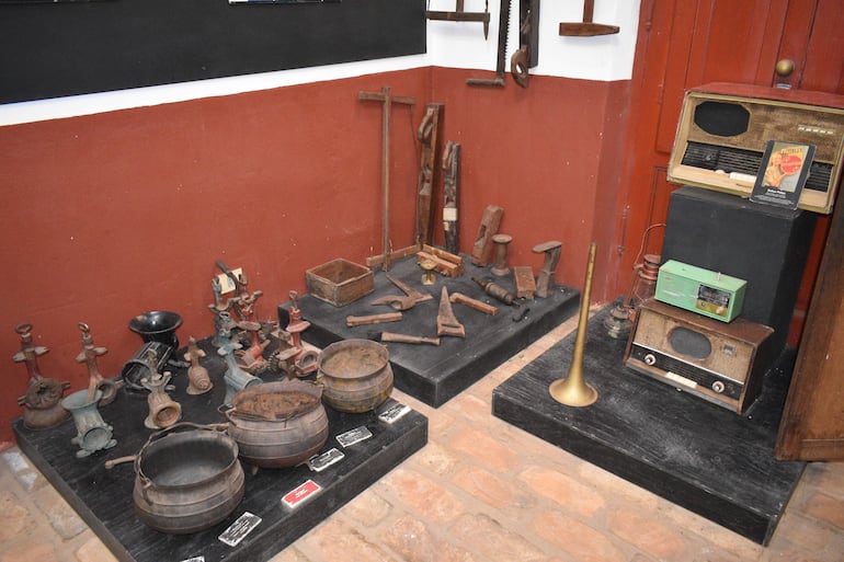 Exhibición de objetos antiguos en un museo con paredes rojas y negras, resaltando herramientas y utensilios históricos.