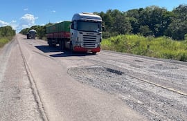 Camión Scania R300 avanza por carretera deteriorada, rodeado de vegetación y bajo un cielo nublado.