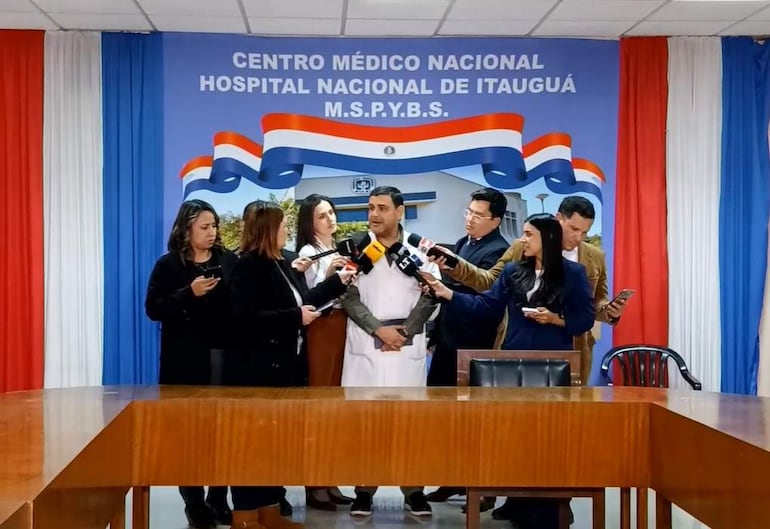 José Espínola Orrego en bata blanca, rodeado de periodistas con micrófonos en el hospital de Itauguá.