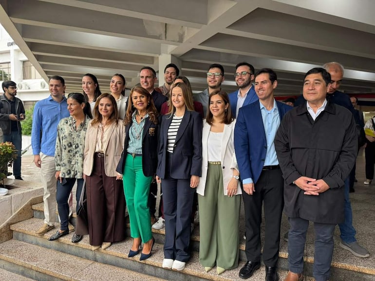 Sole Núñez con traje oscuro sonríe al frente, rodeada de un grupo de personas felices en un evento al aire libre.