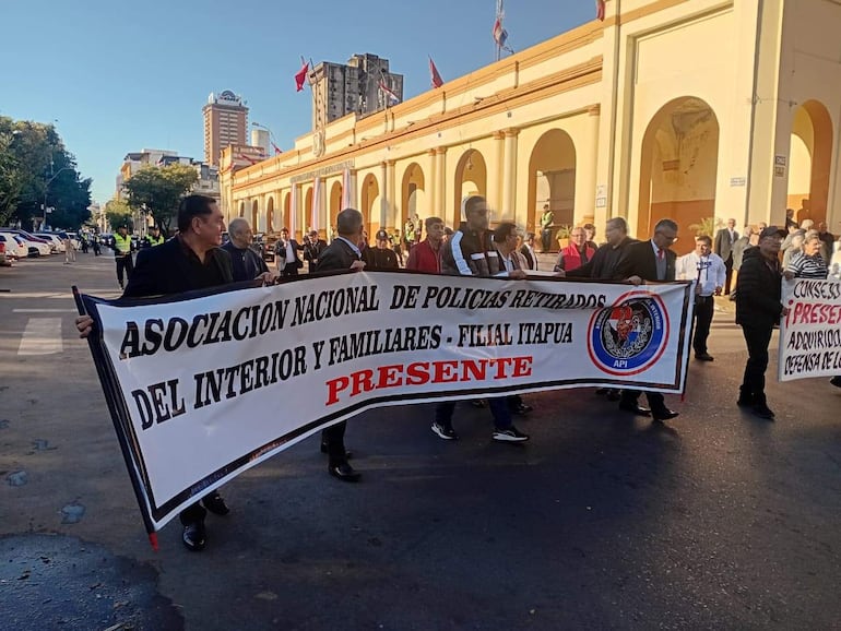 Grupo de hombres con camisas oscuras marchan, sosteniendo un cartel de la Asociación Nacional de Policías Retirados del Interior.