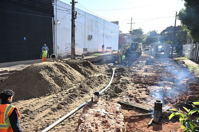 Cinco trabajadores en construcción, uno con chaleco reflectante amarillo, rodeados de maquinaria pesada y tierra bajo un cielo soleado.