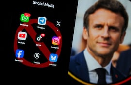Hombre con chaqueta oscura, sobre fondo oscuro, observa una pantalla de móvil con íconos de redes sociales y símbolo de prohibición.