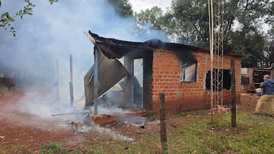 Hombre en chaqueta azul observa daños en edificio de ladrillos, con humo saliendo de su interior y árboles al fondo.