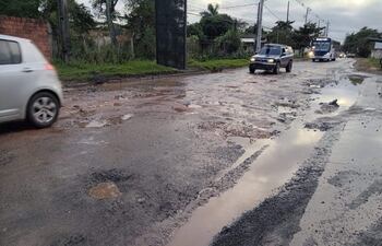 Calle llena de baches y agua, con un automóvil blanco, un SUV oscuro y un autobús en movimiento.