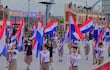 Jóvenes con uniformes formales sosteniendo banderas de Paraguay en el desfile, con expresión seria y un ambiente festivo.