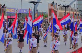Jóvenes con uniformes formales sosteniendo banderas de Paraguay en el desfile, con expresión seria y un ambiente festivo.