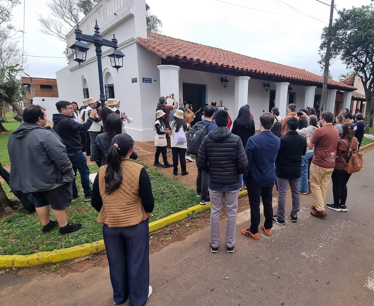 Grupo de personas escuchando atentamente, con algunos utilizando megáfonos, en un entorno colonial y nublado.