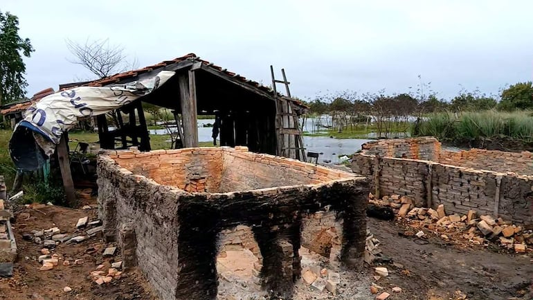 Construcción parcialmente destruida en un entorno rural, con cuerpo de agua al fondo y techo improvisado cubriendo la estructura.
