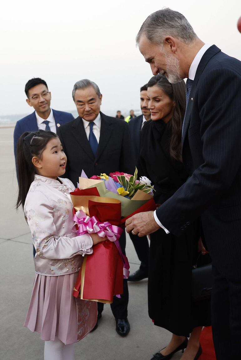 El rey Felipe VI y la reina Letizia reciben flores de manos de una niña a su llegada a China, en el marco de la visita oficial de los reyes de España al país asiático. (EFE/ Chema Moya)
