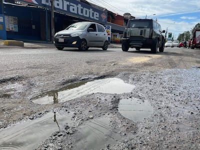 Avenida Santa Teresa con vehículos en movimiento, carretera deteriorada y charcos de agua en un entorno urbano.