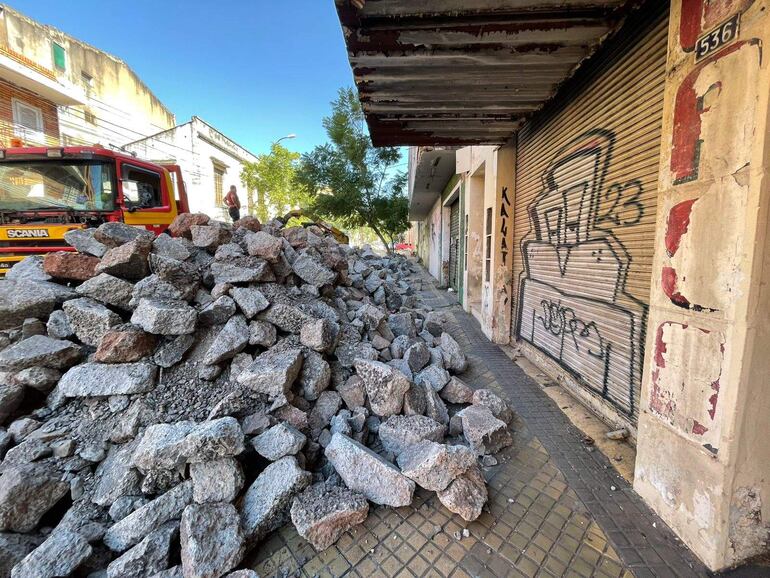 Camión de bomberos Scania estacionado junto a una pila de piedras en una vereda con edificios antiguos y graffitis.