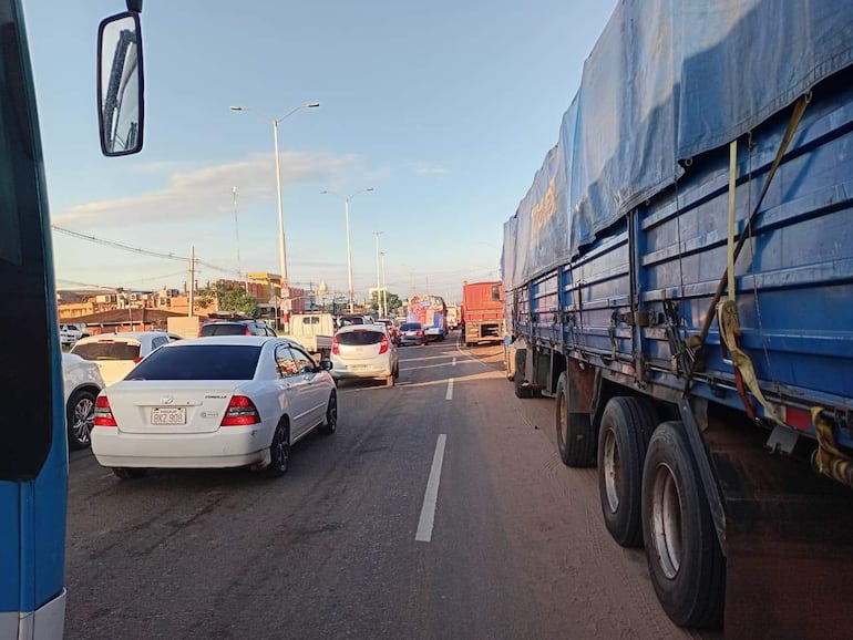 Escena de tráfico con camiones azules y coches alineados en la carretera bajo un cielo despejado.