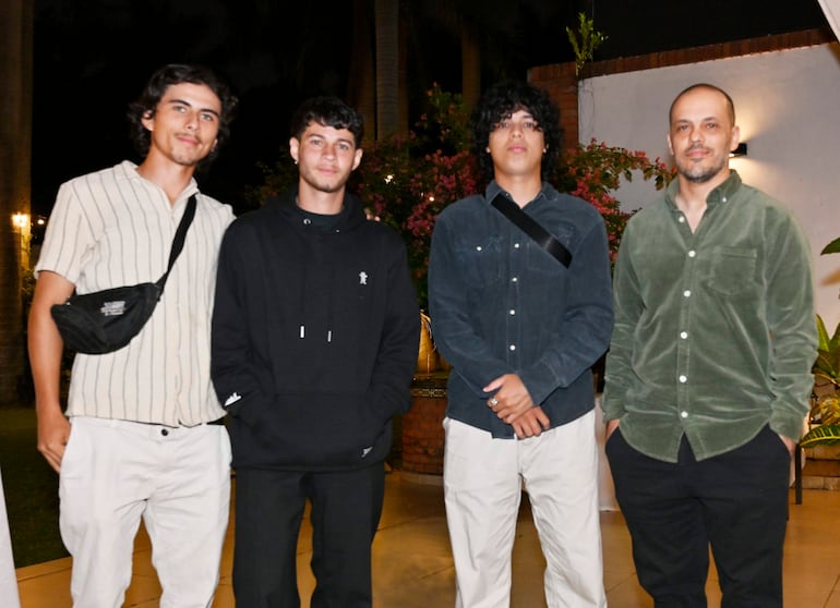 Cuatro hombres posan sonrientes: uno en camisa de rayas clara, otro en sudadera negra, un tercero con camisa azul y el cuarto en camisa verde claro.