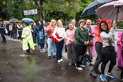 Mujeres en fila bajo la lluvia con paraguas, aguardando para visitar la espada de San Miguel