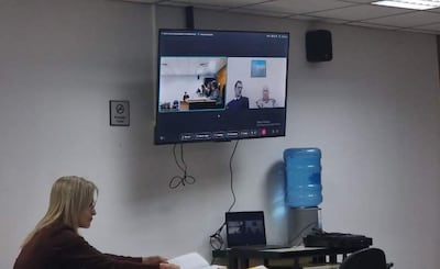 Mujer sentada revisando documentos en una mesa, en ambiente formal y tecnología visible, durante audiencia virtual.