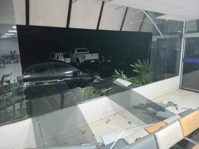 Interior del Instituto Nacional del Cáncer con ventana rota y varios vehículos estacionados en un ambiente desordenado.