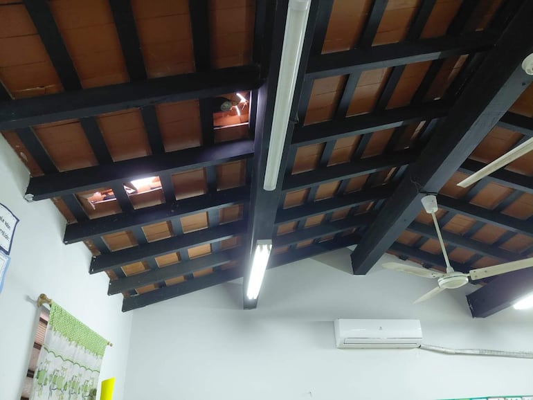 Techo de la Escuela Juan Alberto Samaniego con vigas de madera y tejas terracota, ventilador de techo y cortina decorativa.