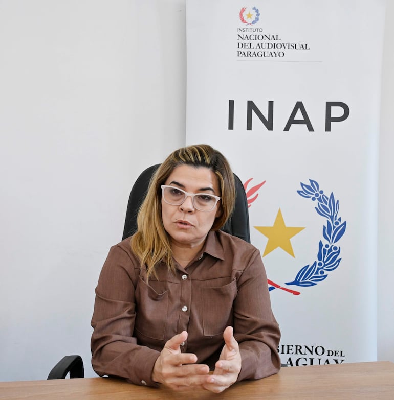 Natalia Fuster con cabello largo y rubio, utiliza gafas gruesas mientras habla en un entorno institucional con una pancarta del INAP en el fondo.