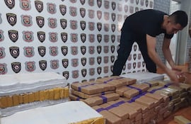 Hombre con camiseta negra y pantalones oscuros, manipulando paquetes sospechosos en un ambiente policial decorado con escudos.