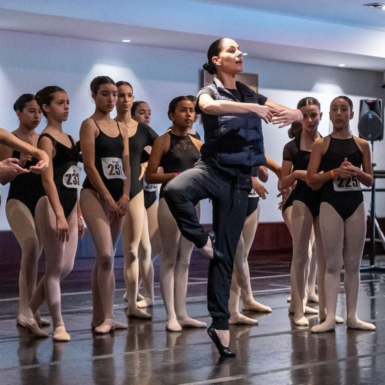Bailarinas en trajes negros y mallas carne, alineadas con una instructora en posición de danza.
