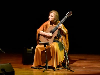 Berta Rojas, con prenda cálida y guitarra, interpreta en un escenario oscuro con luz centrada en ella.